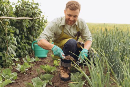 Téléchargez les photos : Homme fermier heureux arrose les lits et travaille dans le jardin - en image libre de droit