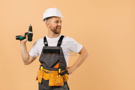 Photo for Positive male repairman at home holding a screwdriver on a beige background - Royalty Free Image