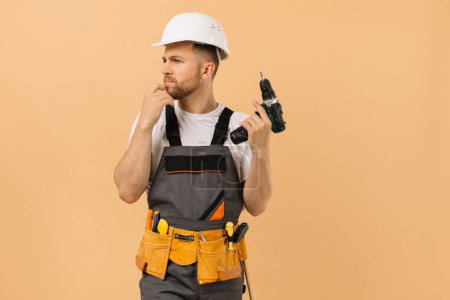 Téléchargez les photos : Réparateur masculin positif à la maison tenant un tournevis et pensant sur un fond beige - en image libre de droit