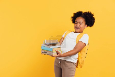 Foto de Feliz colegiala afroamericana sosteniendo cuadernos y libros sobre fondo amarillo, espacio para copiar. - Imagen libre de derechos
