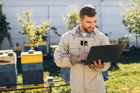 Foto de Hombre agrónomo o ingeniero en traje de protección que trabaja en el ordenador portátil en la granja de abejas - Imagen libre de derechos