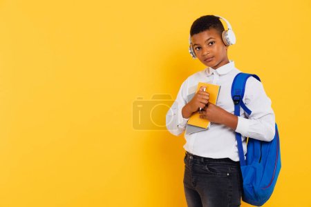 Photo for Happy mixed race schoolboy wearing headphones and backpack holding books and notebooks. Back to school concept. - Royalty Free Image