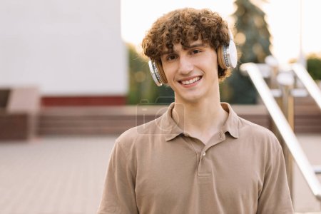 Foto de Retrato de atractivo estudiante masculino de pelo rizado en auriculares sonriendo - Imagen libre de derechos