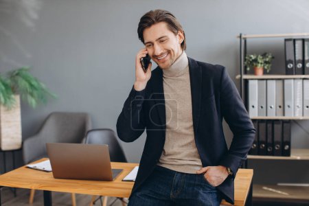 Foto de Hombre de negocios guapo de traje hablando por teléfono en la oficina moderna - Imagen libre de derechos