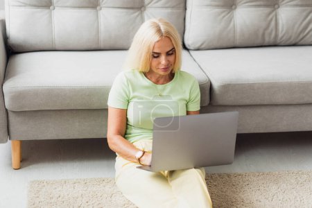 Téléchargez les photos : Attrayant blonde d'âge moyen femme utilise ordinateur portable et appel vidéo - en image libre de droit