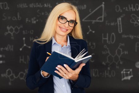 Téléchargez les photos : Portrait d'une enseignante blonde heureuse debout près du tableau noir dans la salle de classe. - en image libre de droit