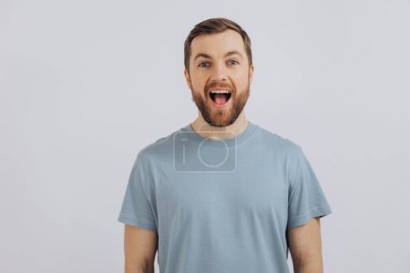 Foto de Retrato de un hombre barbudo moderno de mediana edad con una camiseta azul que muestra emociones sobre un fondo blanco - Imagen libre de derechos