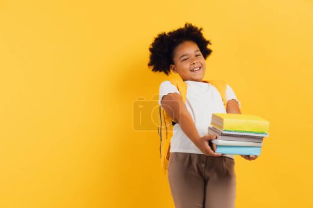 Photo for Happy African american schoolgirl holding notebooks and books on yellow background, copy space. - Royalty Free Image