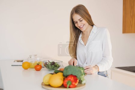 Photo for A cute blonde woman is preparing a salad in the kitchen - Royalty Free Image