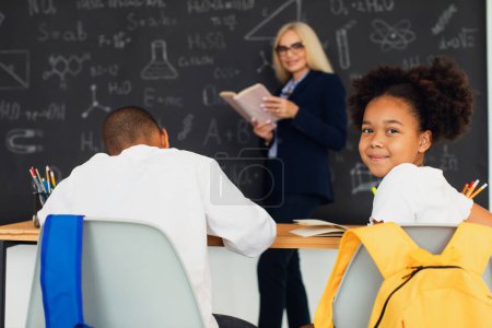 Téléchargez les photos : Portrait d'une écolière afro-américaine assise sur le fond de la salle de classe à la leçon. Retour à l'école. - en image libre de droit