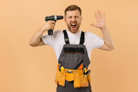 Foto de Reparador masculino positivo en casa con un destornillador pegado a la cabeza y gritando sobre un fondo beige - Imagen libre de derechos