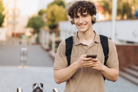 Photo for Attractive curly young man university or college student with phone walking around campus - Royalty Free Image