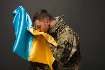Portrait of a courageous Ukrainian military man kissing the flag of Ukraine, the concept of freedom