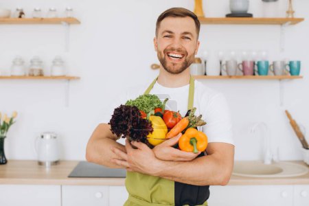 Photo for Portrait of a happy man holding a plate of fresh vegetables in the kitchen - Royalty Free Image