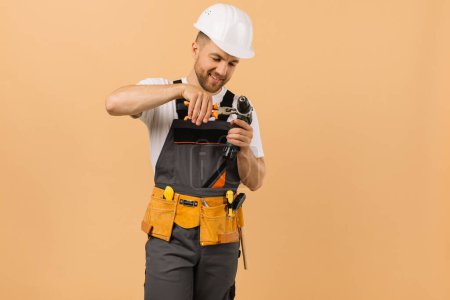 Téléchargez les photos : Réparateur masculin positif à la maison répare quelque chose sur un tournevis sur un fond beige - en image libre de droit