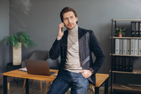 Téléchargez les photos : Beau homme d'affaires en costume parlant au téléphone dans le bureau moderne - en image libre de droit