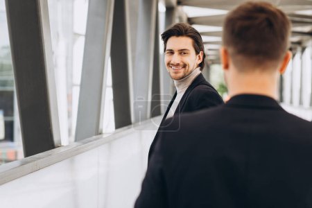 Foto de Dos empresarios modernos se saludan sonriendo y diciendo algo en el contexto de oficinas y edificios urbanos - Imagen libre de derechos