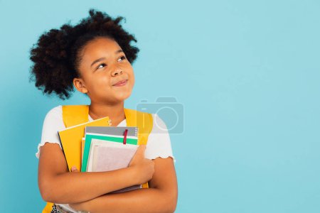 Foto de Feliz colegiala afroamericana sosteniendo libros sobre fondo azul, vuelta al concepto de la escuela. - Imagen libre de derechos