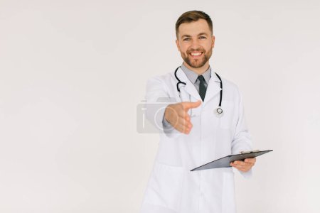 Téléchargez les photos : Le médecin heureux avec un stéthoscope et un dossier étend une main de salutations sur un fond blanc - en image libre de droit