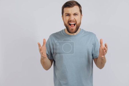 Photo for Portrait of a modern bearded middle-aged man in a blue t-shirt showing anger emotion and screams on a white background - Royalty Free Image