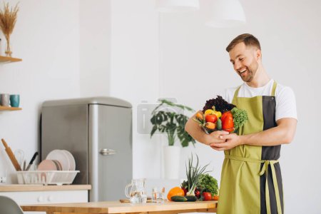 Foto de Retrato de un hombre feliz sosteniendo un plato de verduras frescas en el fondo de la cocina en casa - Imagen libre de derechos
