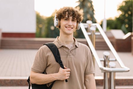Photo for Portrait of attractive curly haired male student in headphones smiling - Royalty Free Image