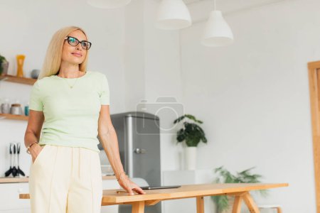 Foto de Moderna atractiva mujer de mediana edad posando en la cocina en casa - Imagen libre de derechos