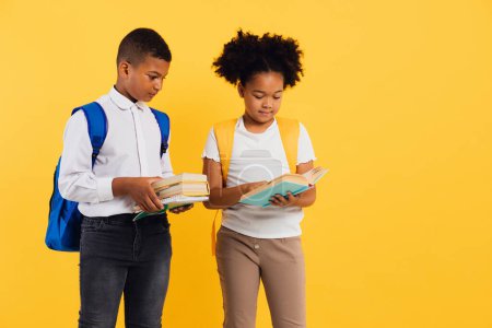 Téléchargez les photos : Heureuse écolière afro-américaine et écolier métis tenant des livres sur fond jaune, espace de copie. - en image libre de droit