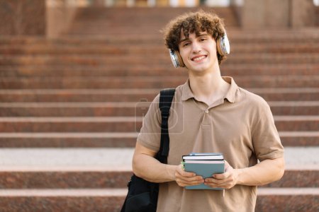 Téléchargez les photos : Portrait d'heureux attrayant étudiant masculin tenant des livres et passé des examens à l'université - en image libre de droit