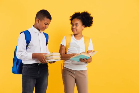 Foto de Feliz colegiala afroamericana y colegial de raza mixta sosteniendo libros sobre fondo amarillo, espacio para copiar. - Imagen libre de derechos
