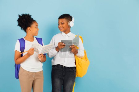Photo for A mixed race schoolboy and an African American schoolgirl are reading an outline together in a school classroom on a blue background, back to school concept. - Royalty Free Image