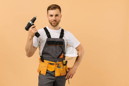 Téléchargez les photos : Le réparateur masculin à la maison tenant un tournevis sur un fond beige - en image libre de droit