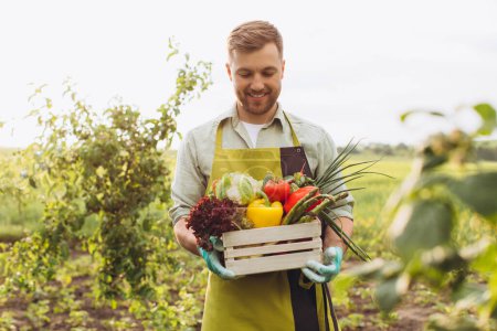 Foto de Hombre agricultor feliz sosteniendo cesta con verduras frescas en el jardín, concepto de jardinería - Imagen libre de derechos