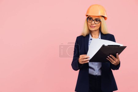 Téléchargez les photos : Portrait de femme d'affaires mature attrayant architecte ou ingénieur dans les lunettes dossier d'utilisation avec des documents sur le fond rose - en image libre de droit