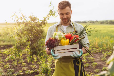 Foto de Hombre agricultor feliz sosteniendo cesta con verduras frescas en el jardín, concepto de jardinería - Imagen libre de derechos