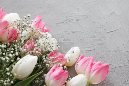 Photo for Pink tulips and white gypsophila flowers bouquet on a stylish gray stone background, selective focus. Mothers Day, birthday celebration concept. Copy space for text - Royalty Free Image