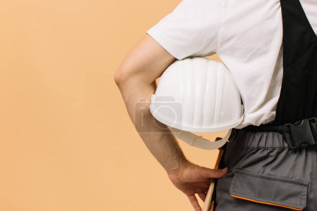 Téléchargez les photos : Homme travailleur de la construction tenant un casque sur un fond beige - en image libre de droit