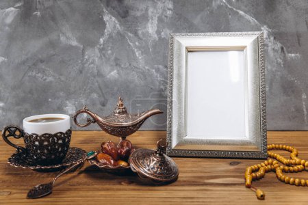 Photo for Composition for Ramadan. Silver frame with copy space or mockup, near traditional islamic tableware with dates and coffee on wooden table. - Royalty Free Image