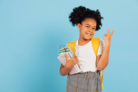 Téléchargez les photos : Heureuse écolière afro-américaine pointant cool sur fond bleu, concept de retour à l'école. - en image libre de droit