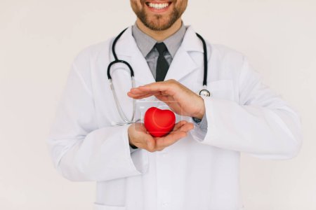 Foto de El médico cardiólogo varón feliz sosteniendo el corazón sobre fondo blanco - Imagen libre de derechos