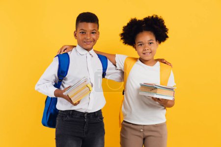 Photo for Happy african american schoolgirl and schoolboy holding books together on yellow background, copy space. - Royalty Free Image
