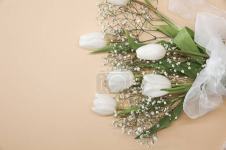Photo for White tulips and gypsophila flowers bouquet on a beige background. Mothers Day, birthday celebration concept. Copy space for text. Mockup - Royalty Free Image