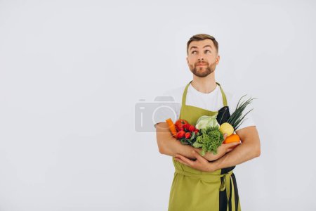 Foto de Hombre feliz sosteniendo muchas verduras frescas diferentes sobre fondo blanco - Imagen libre de derechos