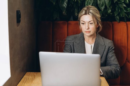 Foto de Madura mujer de negocios administrador de restaurante sentado y trabajando en el ordenador portátil - Imagen libre de derechos