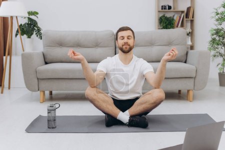Photo for Keep calm on quarantine. Millennial guy meditating with trainer online via laptop connection, empty space - Royalty Free Image