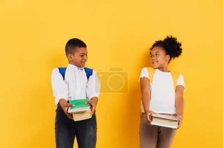 Téléchargez les photos : Heureuse écolière afro-américaine et écolier tenant des livres ensemble sur fond jaune, espace de copie. - en image libre de droit