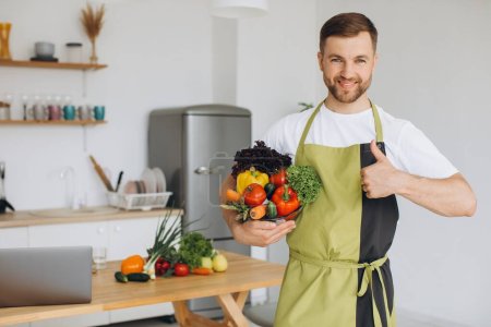 Foto de Retrato de un hombre feliz sosteniendo un plato de verduras frescas en el fondo de la cocina en casa - Imagen libre de derechos