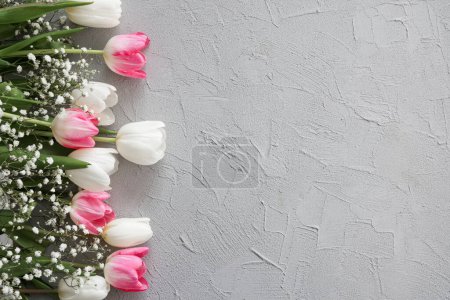 Foto de Tulipanes rosados y ramo de flores de gypsophila blanco sobre un elegante fondo de piedra gris. Día de las Madres, concepto de celebración de cumpleaños. Copia espacio para texto. Burla. - Imagen libre de derechos