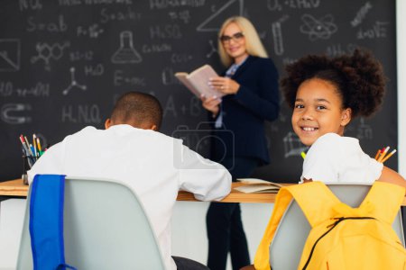 Téléchargez les photos : Portrait d'une écolière afro-américaine assise sur le fond de la salle de classe à la leçon. Retour à l'école. - en image libre de droit