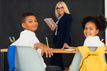 Foto de Una niña y un niño, niños de escuela afroamericanos, resuelven problemas con la maestra durante una lección. Regreso a la escuela. - Imagen libre de derechos